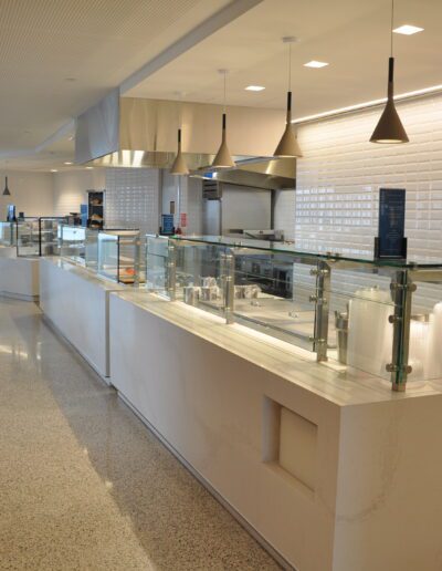 A modern and clean cafeteria counter with a menu board and empty food displays.