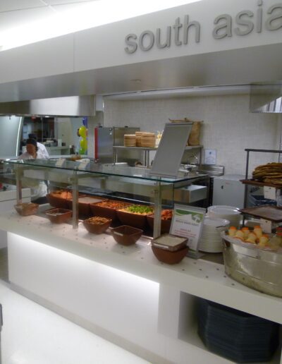 A south asian cuisine station in a cafeteria with a chef preparing food behind a glass partition.