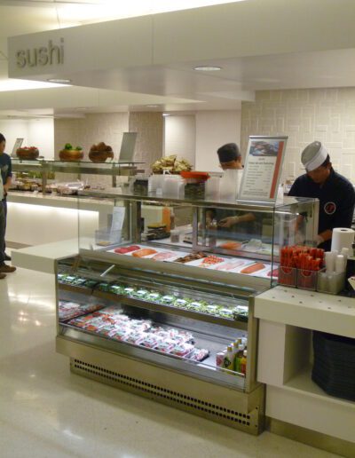 Chefs preparing sushi behind a glass display in a clean and well-organized sushi station.