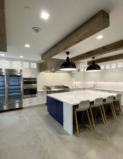 Modern kitchen interior featuring white cabinets, blue island with seating, stainless steel appliances, and exposed wooden beams.