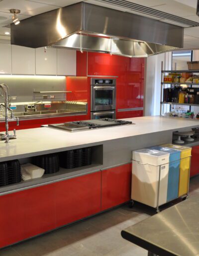 A modern commercial kitchen with stainless steel appliances, red cabinets, and a central prep island.