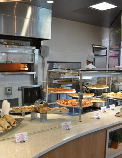 Modern cafeteria serving area with an assortment of pizzas and baked goods on display.