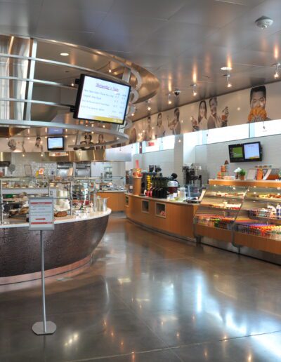A modern cafeteria with food displays and digital menu boards.