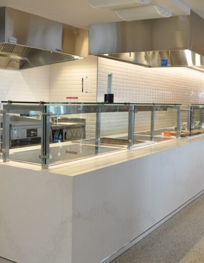 A clean and modern self-service cafeteria counter with food warmers and glass sneeze guards.