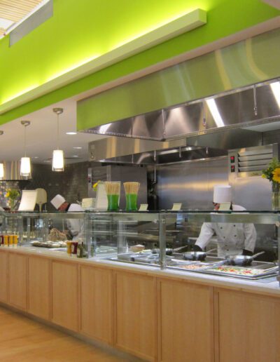 Modern cafeteria with food display counter and a chef at work in the kitchen area.