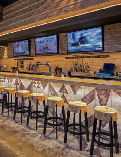 Modern bar with wooden stools and multiple television screens displaying sports channels.